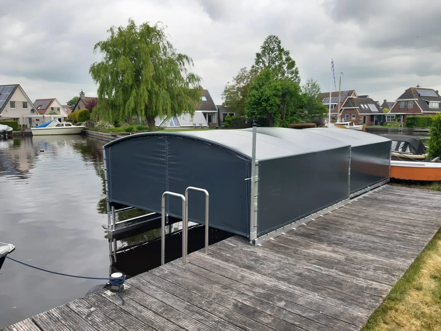 Gesloten donkergrijze bootoverkapping aan een houten steiger